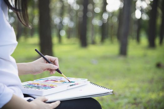 Relax woman painting water colour art work in green garden forest nature - people with creative art in nature stress reduction and meditation concept