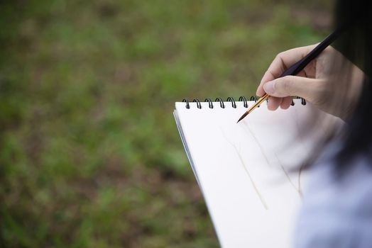 Relax woman painting water colour art work in green garden forest nature - people with creative art in nature stress reduction and meditation concept