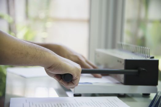 Man making report using comb binding machine - people working with stationary tools concept