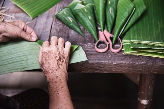 Old grandmother hands working with banana leaf for making flowers container - people making traditional item for local ceremony participation