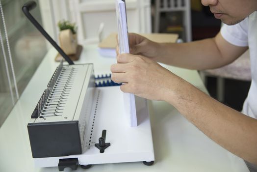 Man making report using comb binding machine - people working with stationary tools concept