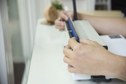 Man making report using comb binding machine - people working with stationary tools concept