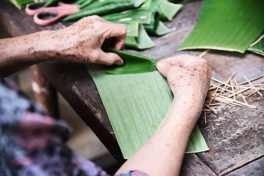 Old grandmother hands working with banana leaf for making flowers container - people making traditional item for local ceremony participation