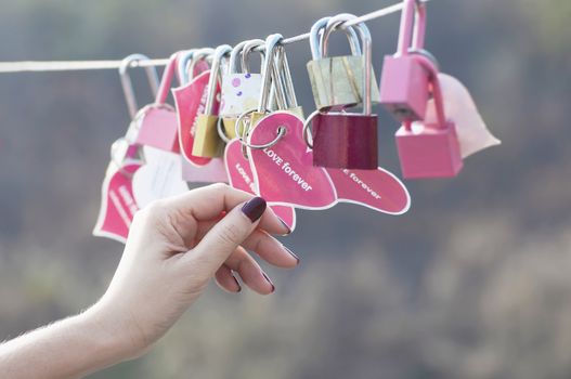 Lady hand holding padlock key with heart symbol of love on bridge - culture of love sign symbol concept