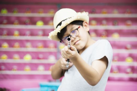 Asian boy happy playing doll gun shoot in local fun park festival event - people with happy activity concept