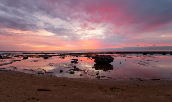 Morning colours of the sunrise paint the sky and reflect in the tidal water. Space for copy. Location: Bateau Bay Australia