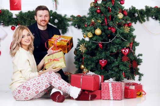 Couple in love sitting next to a nicely decorated Christmas tree, hloding Christmas gifts and smiling