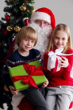 Portrait of smiling little children sitting on santa claus knees near christmas tree