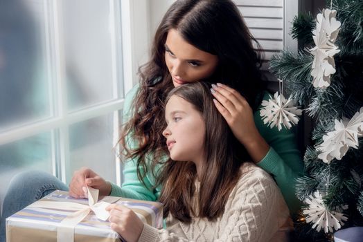 Mother and daughter unwrapping a gift sitting on the floor near christmas tree