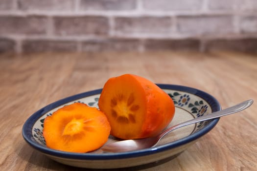 persimmon cut ready to eat, on rustic plate over wooden table with bricks background