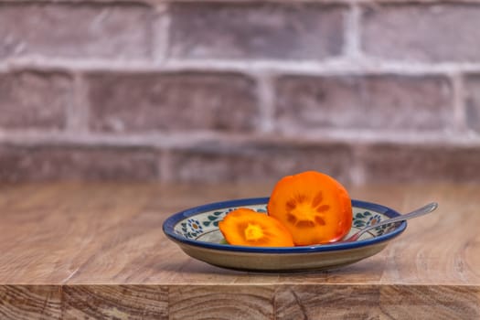 persimmon cut ready to eat, on rustic plate over wooden table with bricks background