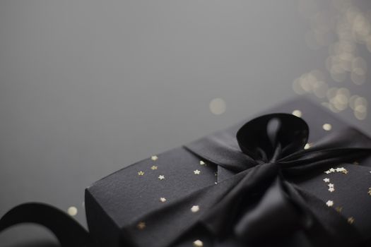Black friday gift, paper box with silk ribbon bow on black paper background with copy space for text