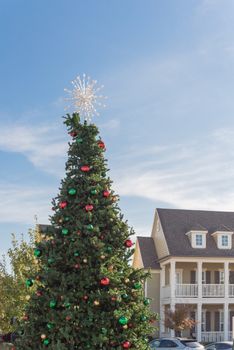 Huge Christmas tree with snowflake tree topper and colorful glass ornaments balls on display at City Square in Coppell, Texas, USA. Christmas decoration row of country-style houses near Dallas