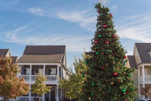 Huge Christmas tree with snowflake tree topper and colorful glass ornaments balls on display at City Square in Coppell, Texas, USA. Christmas decoration row of country-style houses near Dallas