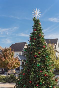 Huge Christmas tree with snowflake tree topper and colorful glass ornaments balls on display at City Square in Coppell, Texas, USA. Christmas decoration row of country-style houses near Dallas