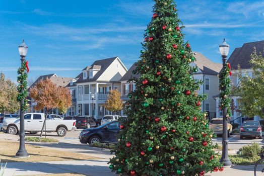 Giant Christmas tree with snowflake tree topper and colorful glass ornaments ball on display at City Square park in Coppell, Texas, USA. Xmas decoration with parked cars and country-style houses