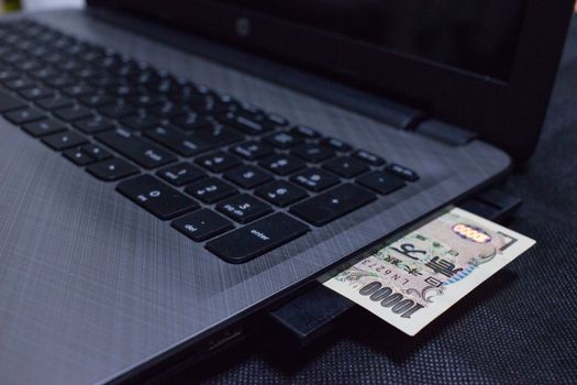 Japanese bank note protruding from a laptop computer.