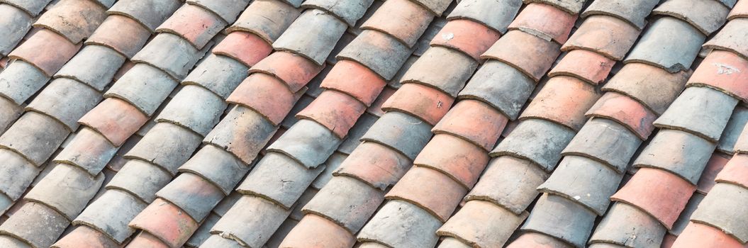 Panorama curved clay tiled roof in various colors from an old house in North Vietnam, late afternoon light. Ancient, weathered roofing surface, moss texture. Natural seamless pattern background