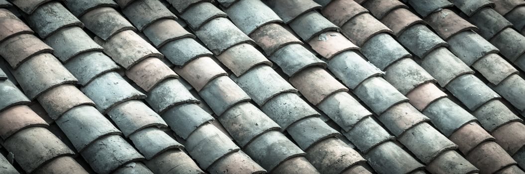 Panorama curved clay tiled roof in various colors from an old house in North Vietnam, late afternoon light. Ancient, weathered roofing surface, moss texture. Natural seamless pattern background