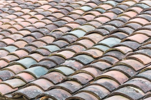 Close-up view curved clay tiled roof in various colors from an old house in North Vietnam, late afternoon light. Ancient, weathered roof tile surface, moss texture. Natural seamless pattern background