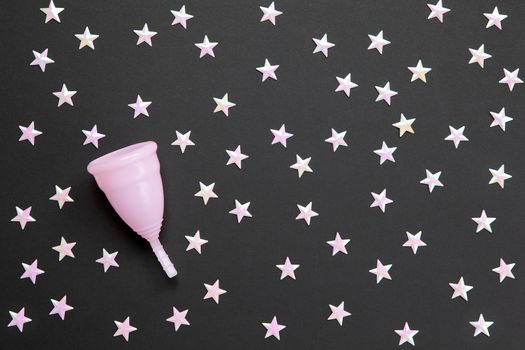 Pink menstrual cup on black background with numerous stars. Concept possibility of use cup at night, zero waste, savings, minimalism. Feminine hygiene product, flat lay, copy space. Horizontal.