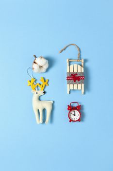 Simple creative Christmas composition. Cotton box, deer, wooden sled, alarm clock on blue background, copy space. Minimal style. Top view. Vertical. For social media, greeting card, office supplies.