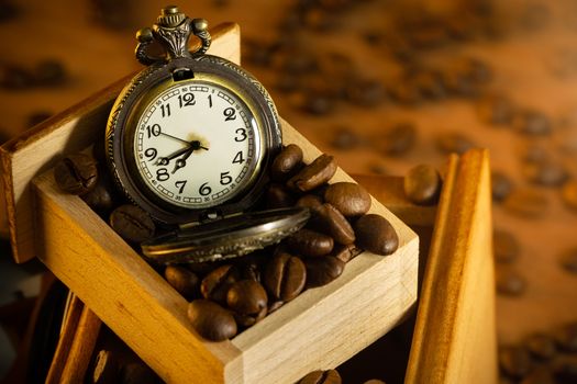 Coffee bean and pocket watch in manual grinder on table. Closeup and copy space. Concept of coffee time in morning.