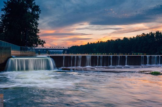 The overflow at Penrith Weir as the sunset colours some of the clouds in the sky and reflects in the rushing waters below.