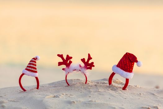 Christmas Santa Hats and reindeer antler headbands standing in the sand on a beach in summer. Beach party, Christmas party.  Copyspace