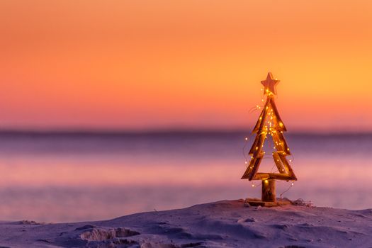 A coastal summer Christmas in Australia.  A driftwood Christmas tree decorated with fairy lights on the beach in summer sunrise or sunset