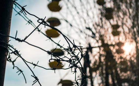 barbed wire on the background of a carousel and the setting sun among the trees in the amusement park in Chernobyl Ukraine in autumn