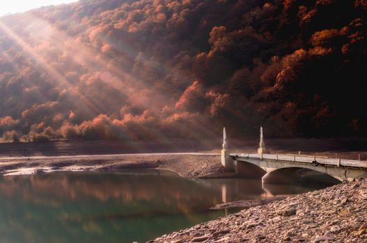 old vintage stone bridge over the river on a background of mountains with trees in Georgia in autumn