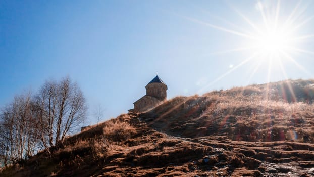 landscape church on the mountain against the background of the sun and sun rays and blue sky in Georgia in the autumn afternoon