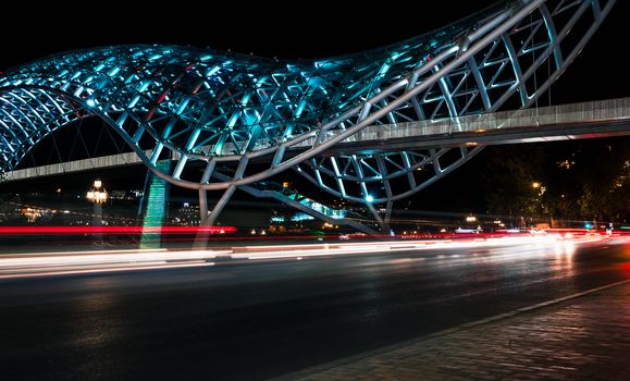 background modern tall bridge with neon light and blurry headlights of a car at night in Tbilisi Georgia