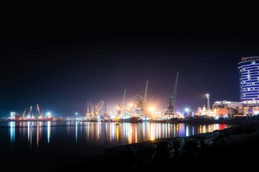 sea ​​port with ships and barges with cranes and neon lights with a building on the pier in Batumi Georgia at night