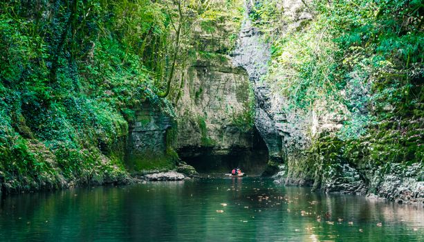 mountain river with tall cliffs and green plants and tourists in a boat in a canyon in Georgia in autumn