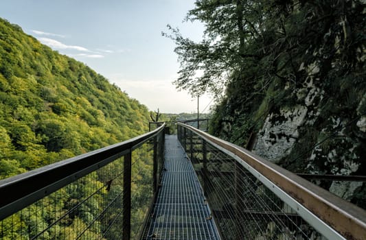 long safe tourist metal bridge in Okatse canyon in Georgia in autumn against mountains and forest and sky with clouds