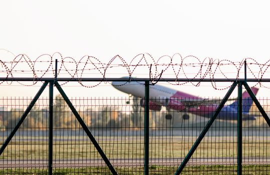flying airliner airplane and a fence with barbed wire and plants and trees