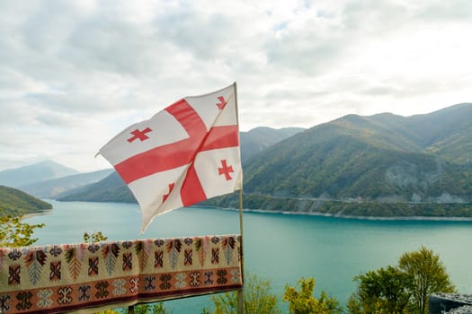 Georgia country flag on the background of a mountain landscape with forest and lake and sky with clouds