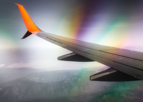 wing of a civilian airliner in flight above clouds and mountains with color optical effect