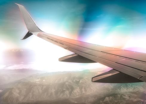wing of a civilian airliner in flight above clouds and mountains with color optical effect