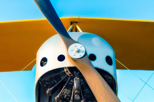 propeller with engine and yellow wings of a vintage airplane on a blue background close up