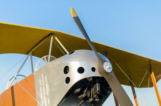 cockpit with an engine with a propeller and wings of a yellow vintage airplane against a blue sky close up in isolation