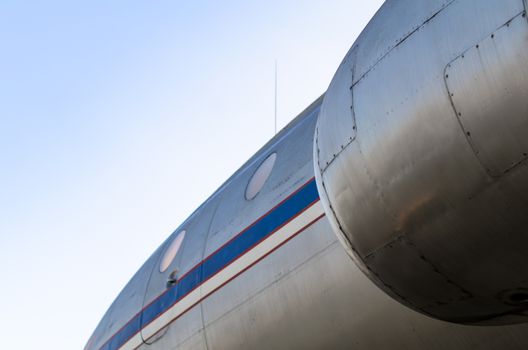 background airplane body with blue and white stripe with portholes and turbine close up