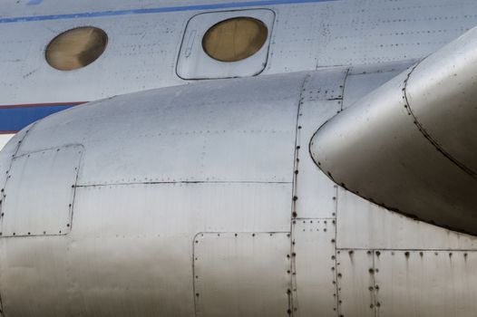 part of the airplane with portholes and a turbine with blue stripes close up