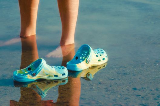 rubber slippers float in clear water next to female legs closeup
