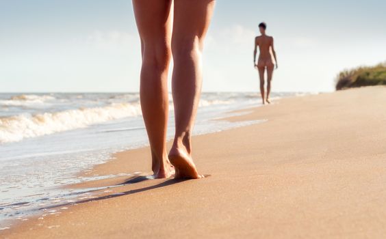 nude young girls walk on the beach in the waves of the surf on a summer day
