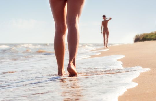 nude young girls walk on the beach in the waves of the surf on a summer day