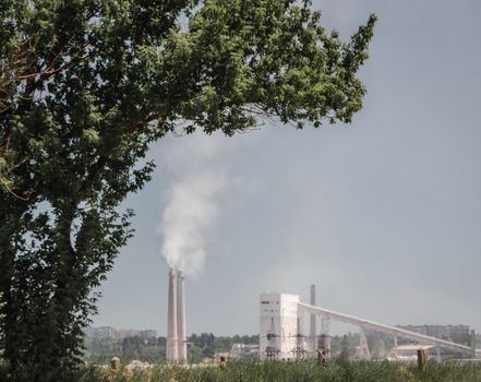 factory with smoking pipes on a background of a tree with green leaves