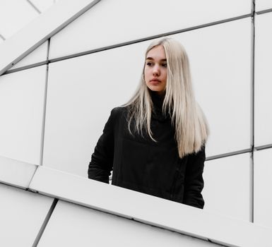 young blonde girl in black clothes against a gray building